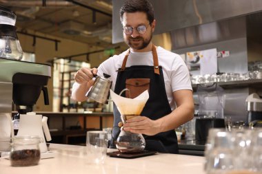 Barista kahve makinesinde kahve yapıyor. Kafedeki masada kağıt filtresi var.