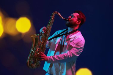 Mavi arka planda bulanık ışıklarla saksafon çalan profesyonel bir müzisyen. Bokeh etkisi