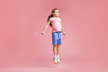 Açık pembe arka planda ip atlayan sevimli küçük bir kız.