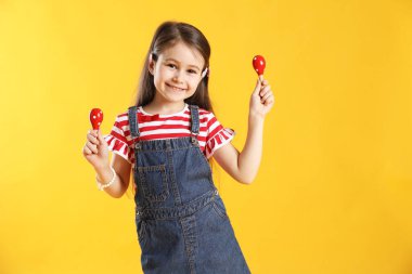 Sarı arka planda oyuncak marakas oynayan tatlı kız.