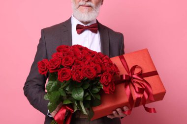 Kırmızı gül buketi ve pembe arka planda hediye kutusu olan son sınıf öğrencisi.