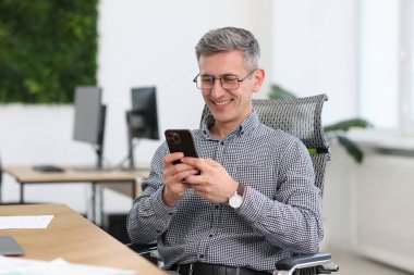 İş yerinde akıllı telefonuyla gülümseyen bir işadamı.