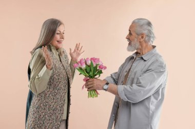 Adam bej arka planda mutlu karısına pembe lale buketi sunuyor.