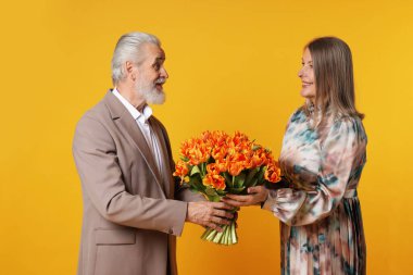 Adam sarı arka planda mutlu karısına bir buket lale sunuyor.