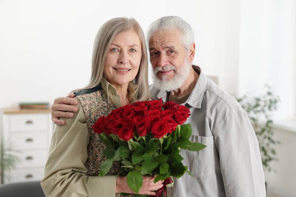 Happy couple with bouquet of red roses at home