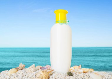 Bir şişe güneş kremi ve okyanus kıyısında deniz kabukları.