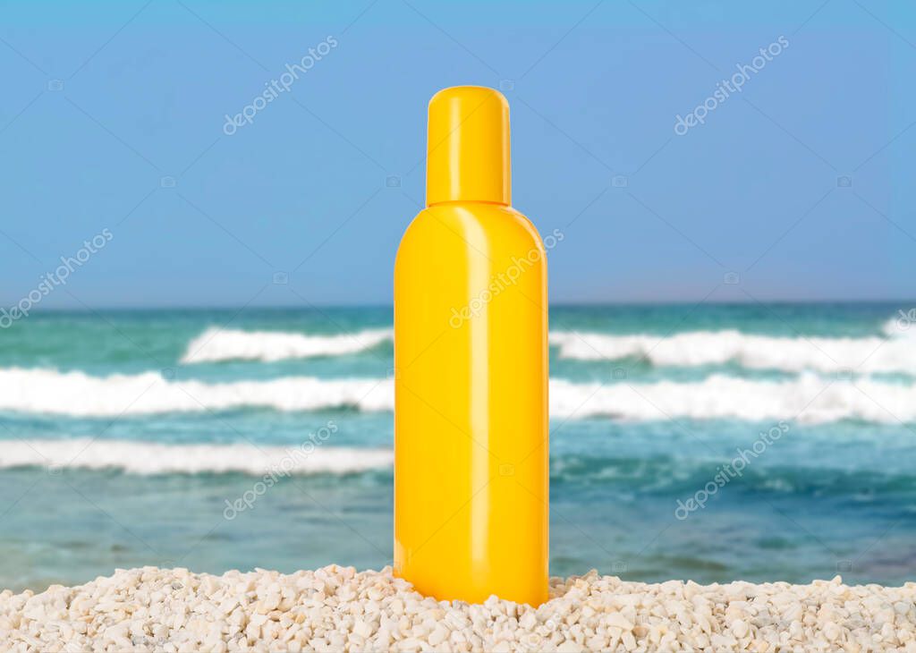 Bottle of sunscreen product on beach near ocean