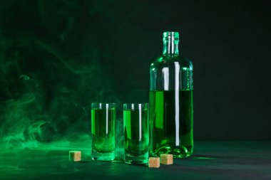 Absinthe shot bardakları, şişe ve esmer şeker siyah arka planda dumanlı