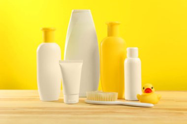 Baby cosmetic products and bath accessories on wooden table against yellow background