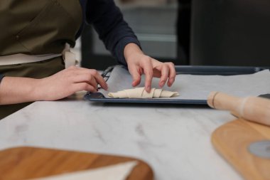 Beyaz mermer masadaki pişirme örtüsüne çiğ kruvasan koyan kadın, yakın plan.