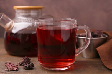 Cam fincanda leziz amber çayı, çaydanlık ve ahşap masada kuru gül sepalleri, yakın plan.