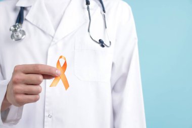 Çoklu Skleroz farkındalığı. Açık mavi arka planda turuncu kurdeleli doktor, yakın plan.