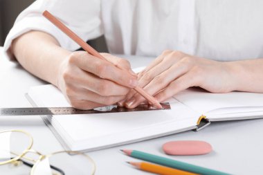 Beyaz masadaki deftere cetvel ve kalemle çizim yapan kadın, yakın plan.