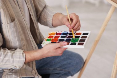 Sulu boyalı ve fırçalı genç bir adam sanatçının stüdyosunda, yakın plan.