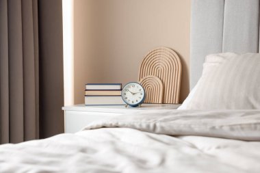 Yatağın yanında kitap, dekor ve alarmlı bir masa var.