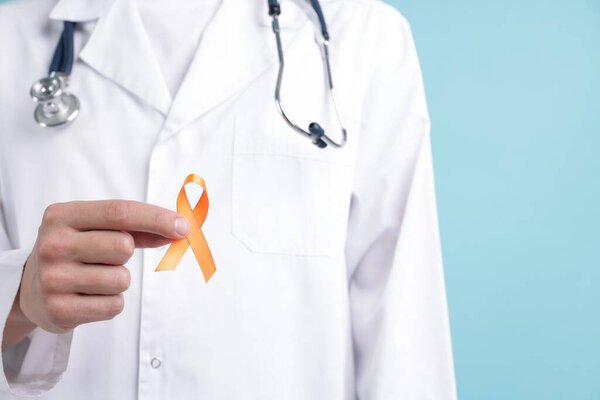 Multiple Sclerosis awareness. Doctor with orange ribbon on light blue background, closeup