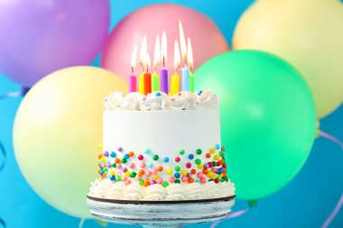 Enfes bento keki serpiştirilmiş, yanan mumlar ve açık mavi arka planda renkli balonlar, yakın plan.