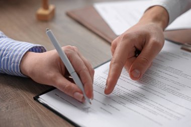 Belgeye işaret eden noter ve müşteri, kapalı oturulan ahşap masaya imza atıyor, yakın plan