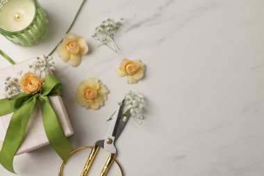 Çiçekçi. Kutu, çiçekler, kurdele, yanan mum ve makas beyaz mermer masada, düz yerde. Metin için boşluk