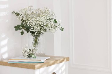 Evdeki masasında okaliptüs dalları vazoda ve dergiler olan güzel gypila çiçekleri. Metin için boşluk