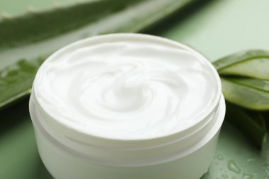 Aloe vera özütüyle nemlendirici krem, yeşil arkaplanda yapraklar ve su damlaları, yakın plan
