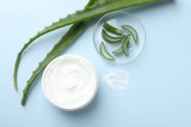 Aloe vera özütüyle nemlendirici krem ve açık mavi arkaplanda yapraklar, düz bir zemin.