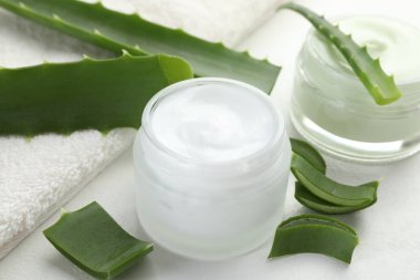 Aloe vera özütüyle nemlendirici krem, beyaz desenli arka planda yapraklar ve havlu, yakın plan