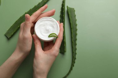 Yeşil arka planda nemlendirici krem ve aloe vera yaprakları olan bir kadın. Metin için boşluk