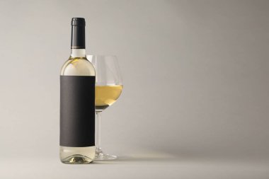 Bardakta lezzetli beyaz şarap ve açık gri arka planda şişe, metin için yer