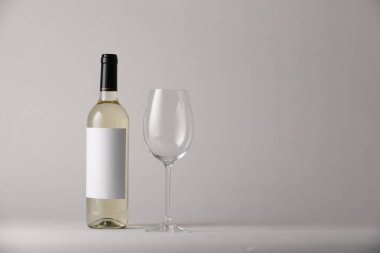Bardakta şarap ve açık gri arka planda şişe, metin için yer var.