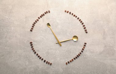 Kahve çekirdekleri ve kaşıklar gri masada saati temsil ediyor.