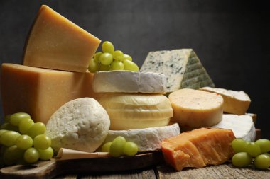 Ahşap masadaki farklı peynir ve üzüm türleri koyu arkaplan ve yakın plan