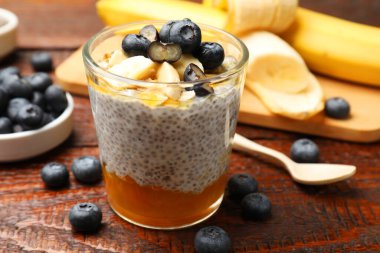 Delicious chia pudding with blueberries and banana in glass on wooden table, closeup