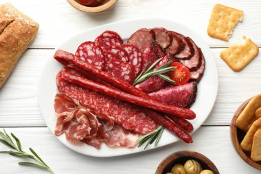 Farklı tütsülenmiş sosisler beyaz ahşap masada servis edilir.