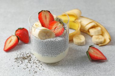 Çilekli lezzetli chia pudingi ve açık gri masada muz, yakın plan.