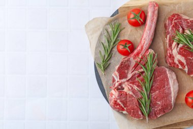 Çiğ et parçaları, biberiye ve domatesler beyaz fayanslı masa, üst manzara. Metin için boşluk