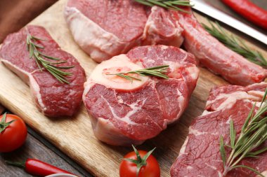 Çiğ et parçaları, biberiye ve domatesler ahşap masada, yakın plan.