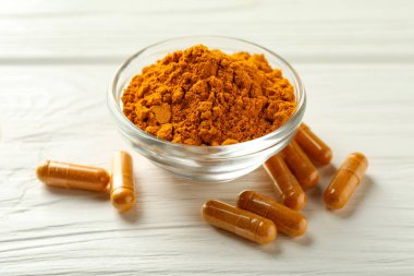 Beyaz ahşap masanın üzerinde zerdeçal kapsülleri ve toz, yakın plan.