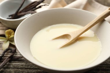 Lezzetli yoğunlaştırılmış süt, kaşık, vanilya kabukları ve çiçek ahşap masada, yakın plan.