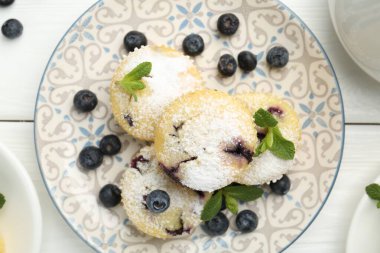 Yaban mersinli leziz çörekler, pudra şekeri ve beyaz ahşap masa üzerinde nane şekeri.