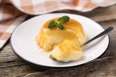 Karamel soslu lezzetli puding ve ahşap masada servis edilen nane, yakın plan.