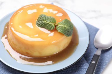 Karamel soslu lezzetli puding ve beyaz masada nane şekeri, yakın plan.