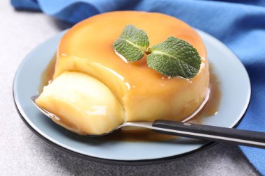Karamel soslu lezzetli puding, gri desenli masada nane ve kaşık, yakın plan.