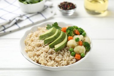 Lezzetli kahverengi pirinç, kasede sebzeler, beyaz tahta masa, yakın plan.