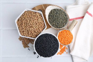 Beyaz fayanslı masa üzerinde farklı mercimek türleri, üst görünüm