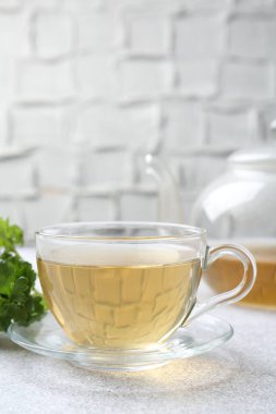 Cam bardakta Aromatik bitki çayı, taze maydanoz ve açık gri masada çaydanlık, yakın plan.