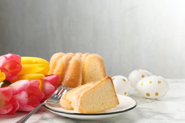 Lezzetli kek parçaları, Paskalya yumurtaları ve laleler açık mermer masada.