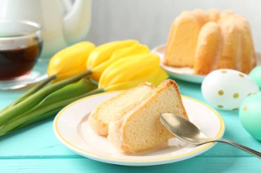 Lezzetli kek parçaları, Paskalya yumurtaları, laleler ve çay açık mavi ahşap masada, yakın plan.