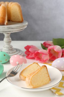 Lezzetli kek parçaları, beyaz ahşap masada paskalya yumurtaları ve laleler.