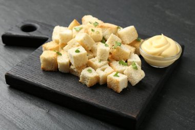 Kesilmiş maydanozlu ve soslu çıtır kıtır ekmek, koyu dokulu masa, yakın plan.